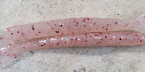 Soft plastic lure glows in the dark, pink and white, with glitter. Fishing lure that is two tone.